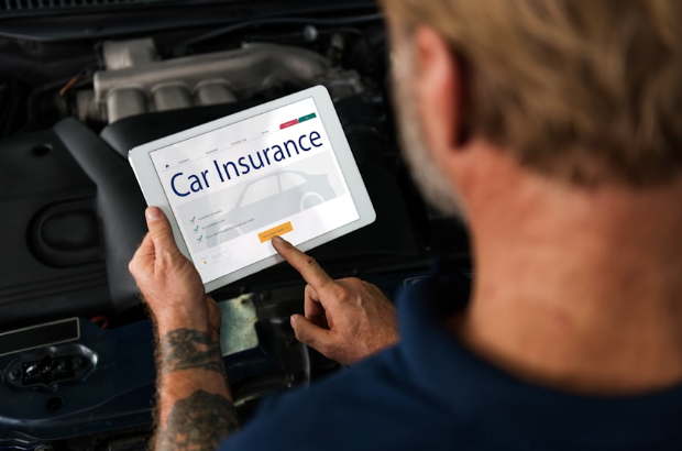 A close-up shot of a person sitting in a car holding a digital tablet that reads "CAR INSURANCE" on the screen. The person is facing away from the camera, and their finger is hovering over a button on the screen that reads "Get a Quick Quote."